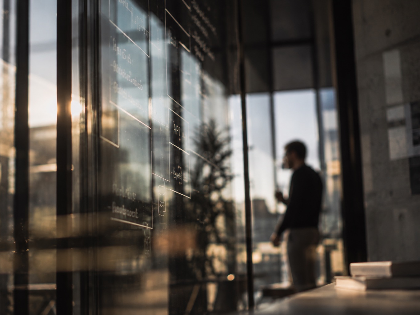 Architecture diagram drawn on a glass wall, with a blurred person standing against the light in the background